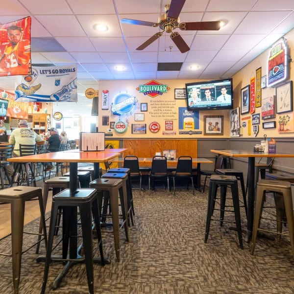 A casual Pizza Shoppe dining area with high-top tables, bar stools, sports memorabilia, and a TV.