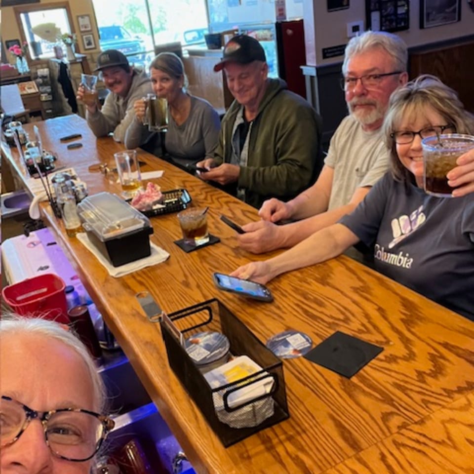 A group of people enjoying drinks and conversation at a wooden bar counter.
