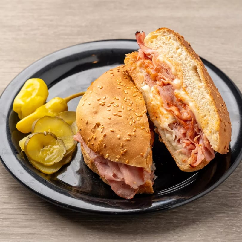 A sliced ham and cheese sub sandwich with pickles and banana peppers on a black plate.