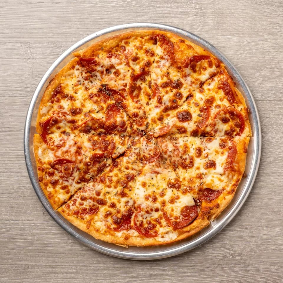 A whole pepperoni pizza, cut into slices, on a metal pan atop a wooden table.