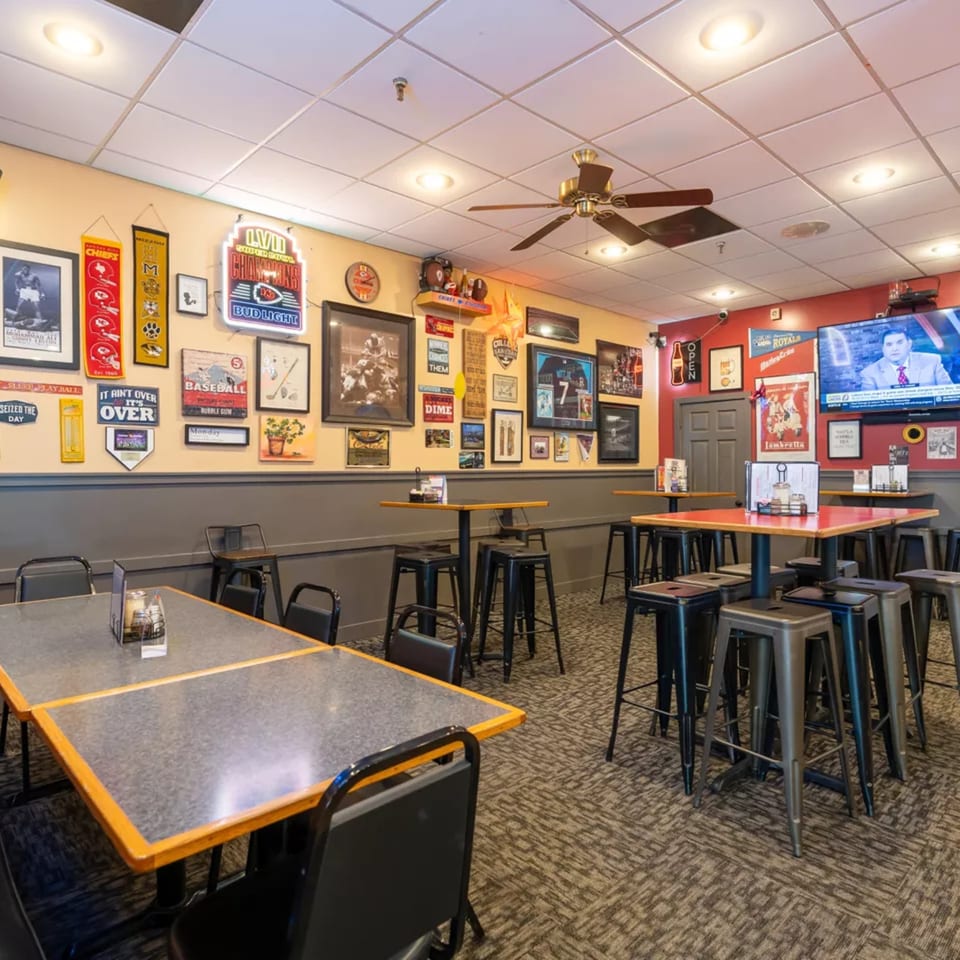 Interior of Pizza Shoppe with sports memorabilia, high-top tables, and a TV showing a news broadcast.