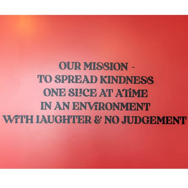 Pizza Shoppe's mission statement on a red wall: "To spread kindness one slice at a time."