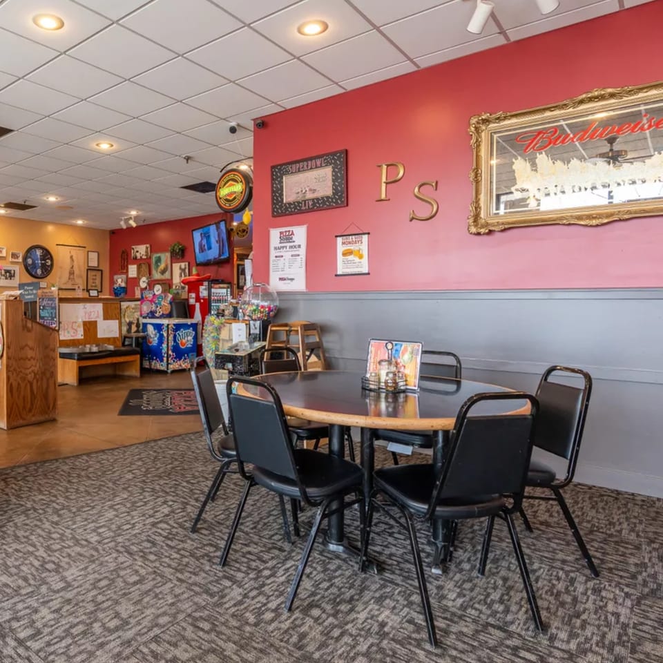 Interior of Pizza Shoppe with a round table and chairs in the foreground, and red walls.