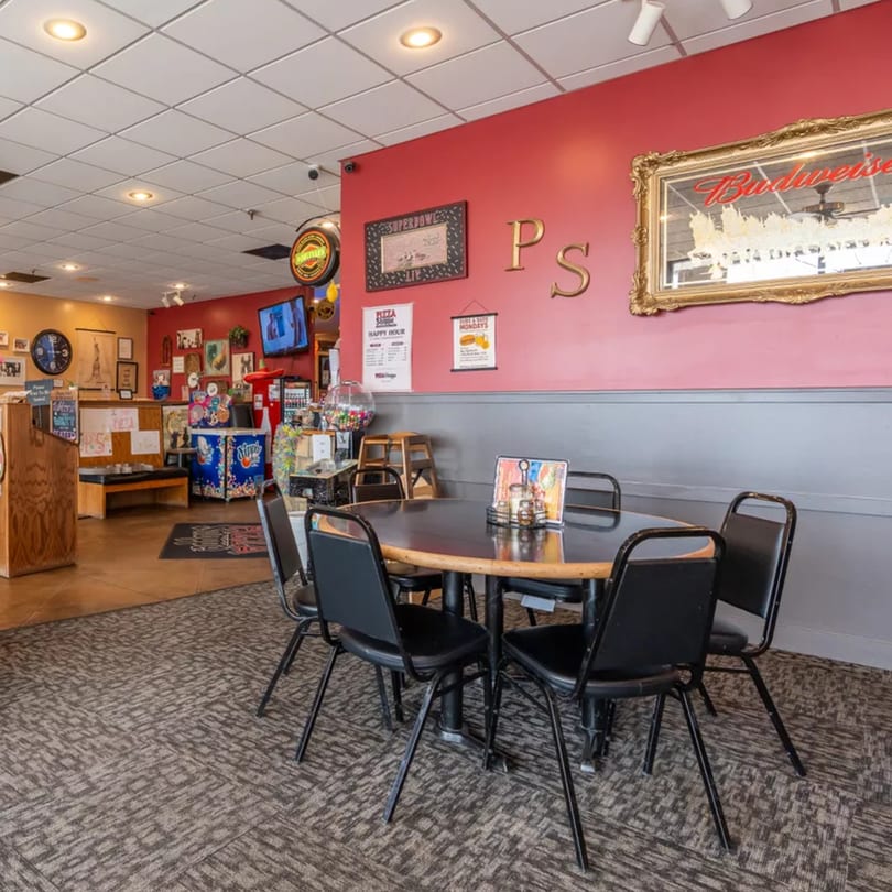 Interior of Pizza Shoppe with a round table and chairs in the foreground, and red walls.