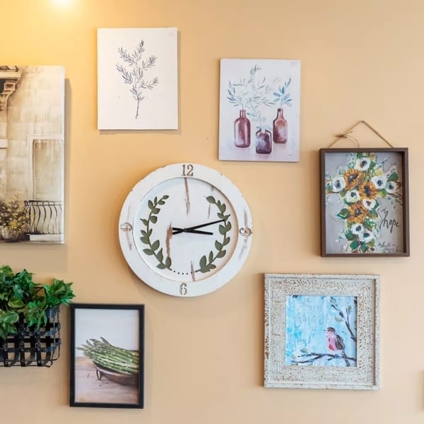 A gallery wall with various framed art, a white clock, and a hanging plant on a peach-colored wall.