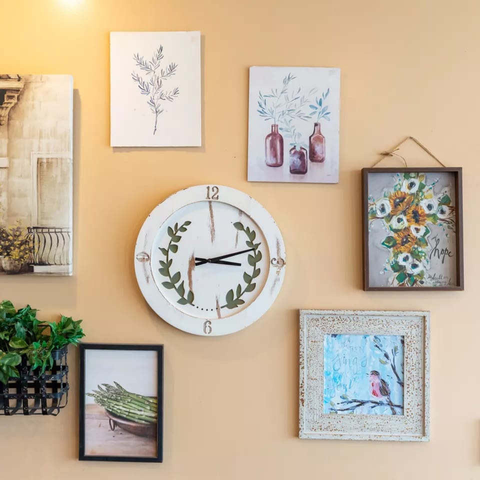 A gallery wall with various framed art, a white clock, and a hanging plant on a peach-colored wall.