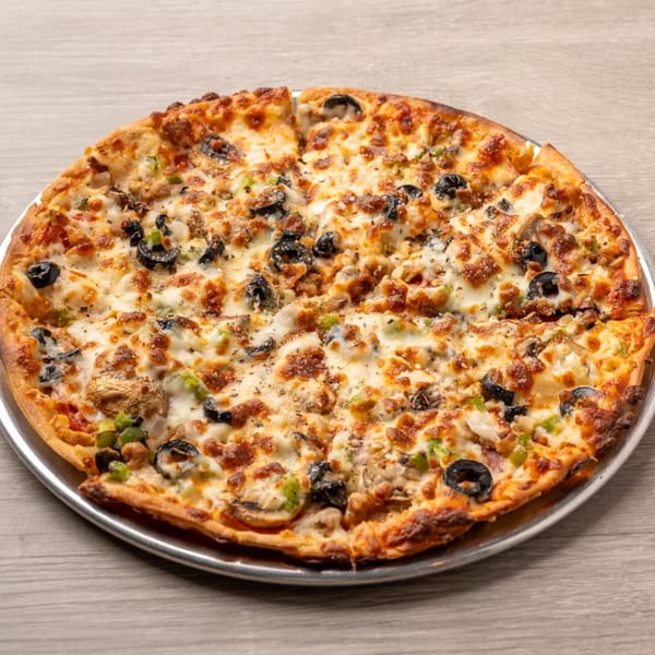 A freshly baked Pizza Shoppe pizza with olives, mushrooms, and green peppers on a metal pan.