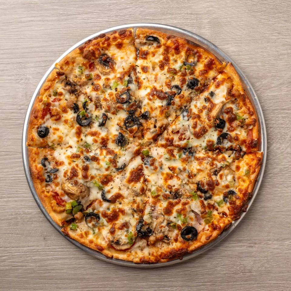A whole pizza with melted cheese, black olives, mushrooms, and green peppers on a metal pan.
