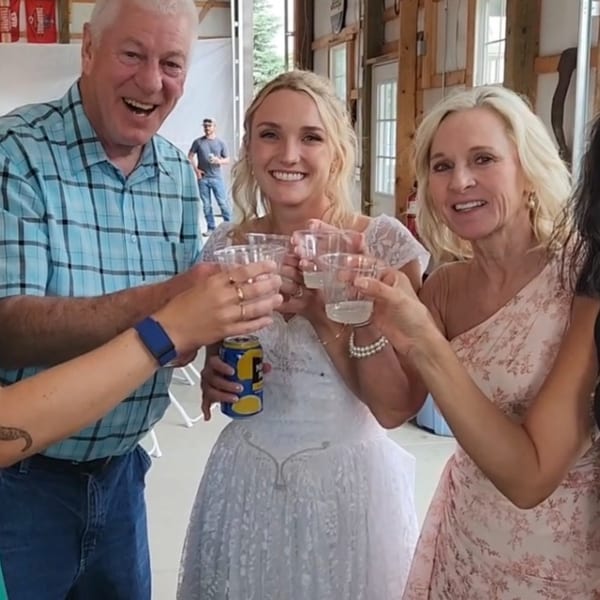 Three smiling people, two women and one man, clinking plastic cups and a beer can in a toast.