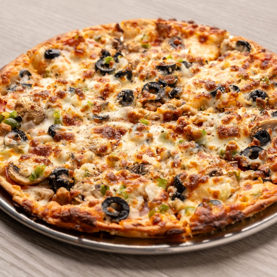 A freshly baked pizza with black olives, mushrooms, and green peppers on a metal pan.