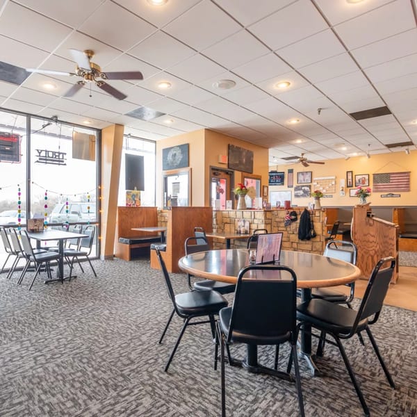 Interior of Pizza Shoppe with tables, chairs, booths, and American flag decor on the walls.
