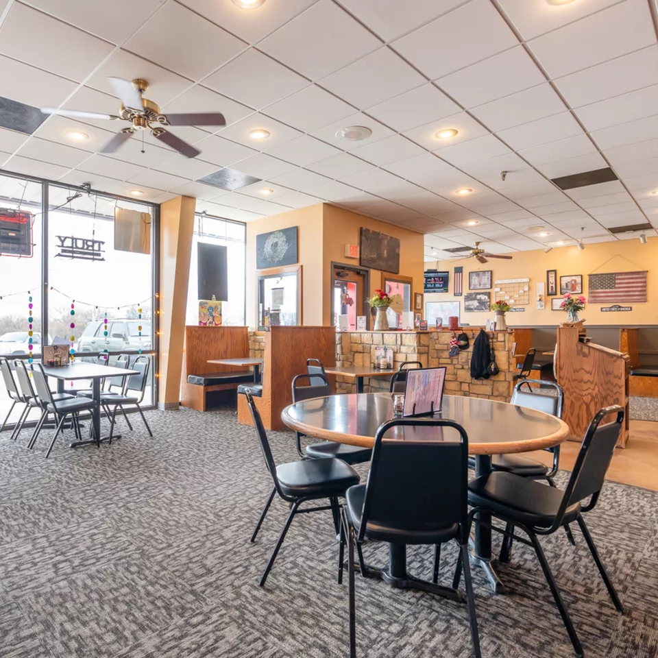 Interior of Pizza Shoppe with tables, chairs, booths, and American flag decor on the walls.